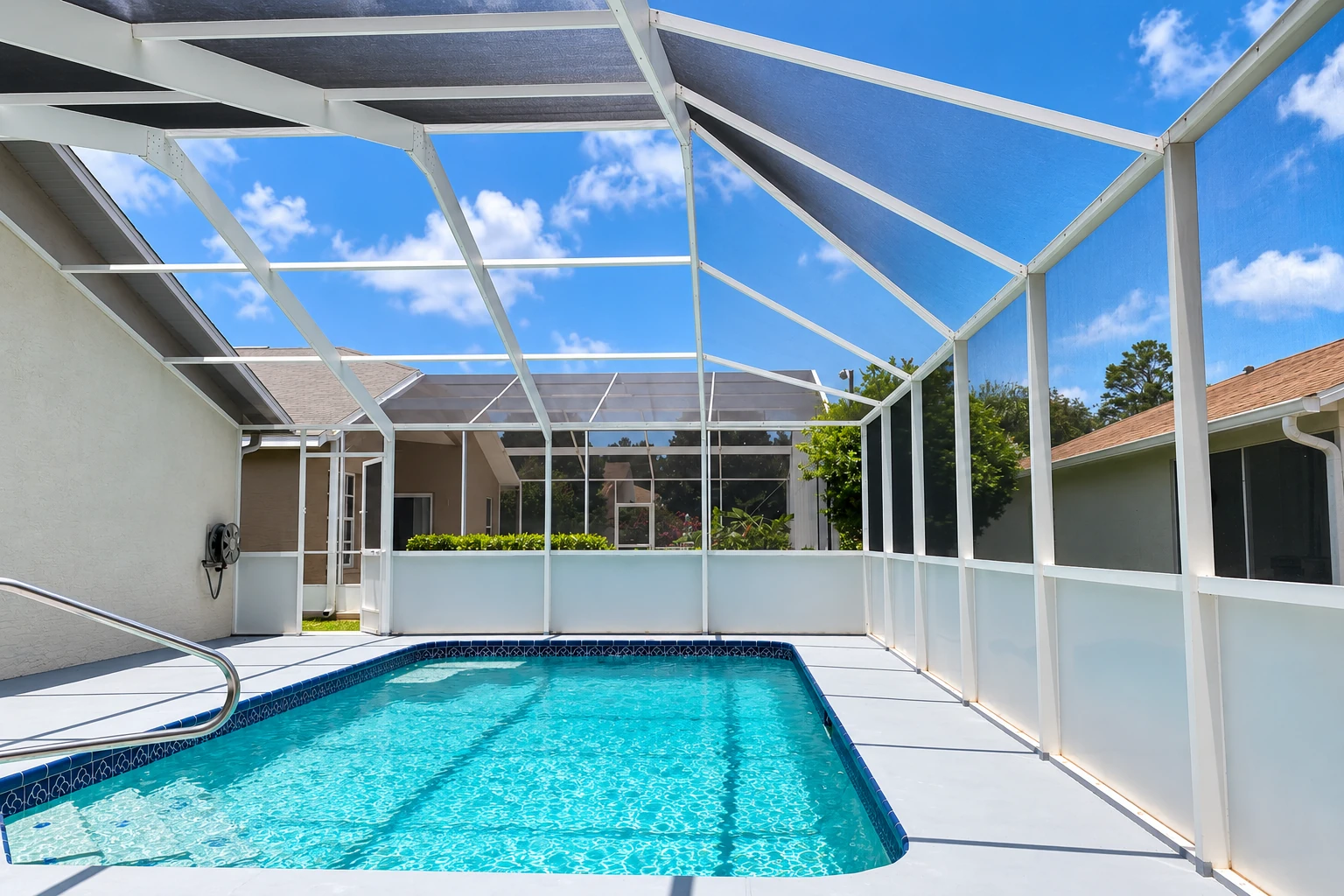 Enclosed patio pool beneath a white-framed screen roof, with translucent lower panels and a clear blue sky.