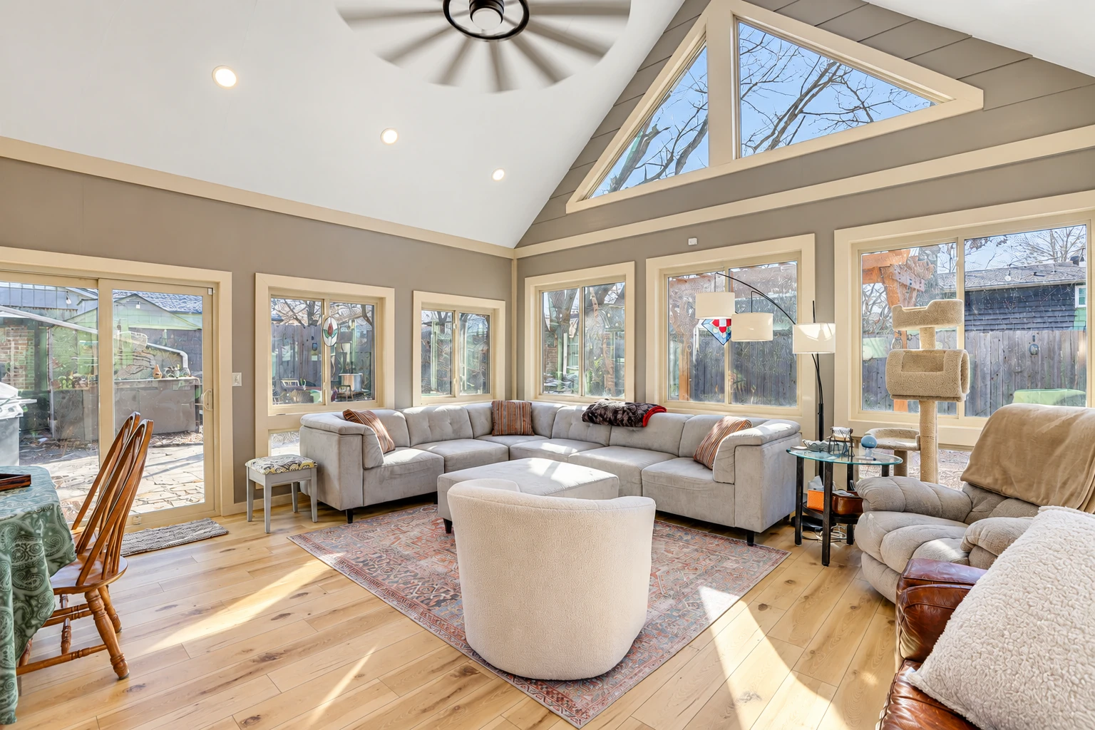 Four-season sunroom with a vaulted ceiling, large windows, a sectional sofa, and light wood flooring.