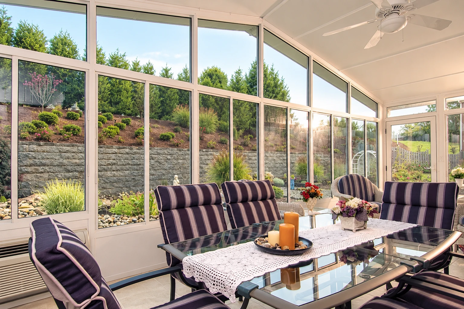 Sunroom with white-framed windows, striped seating, and a glass dining table overlooking a landscaped garden.